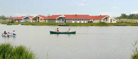 A calm lake with a row of houses with red roofs in the background.