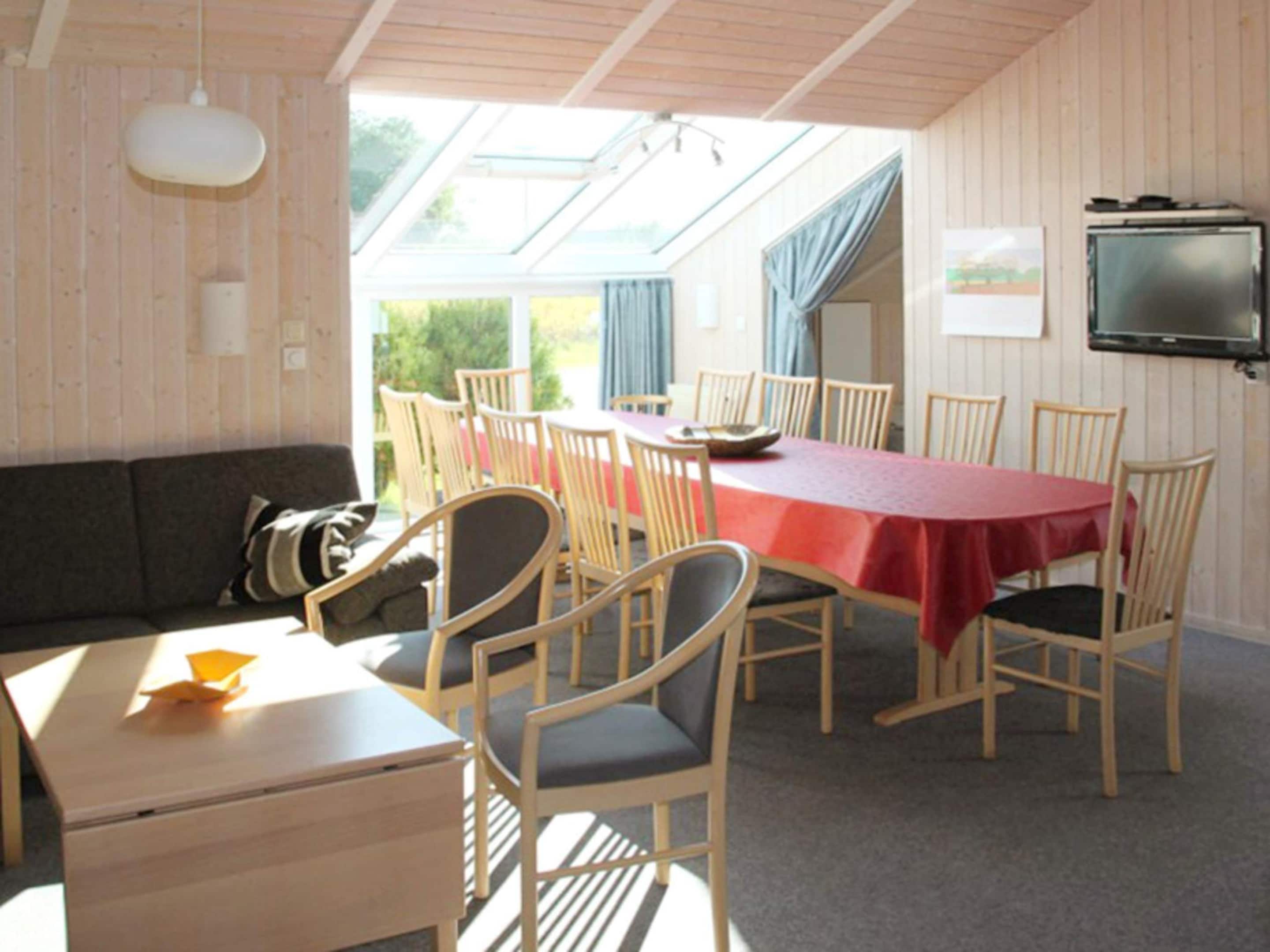 Uma sala de jantar com uma mesa comprida, cadeiras, um sofá e uma televisão.
