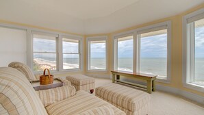 A beach view room with large windows, a sofa, a bench, and a wicker basket.