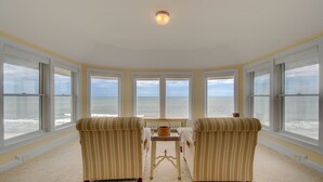 A room with large windows offering ocean views, two armchairs, a small table, and a ceiling light.
