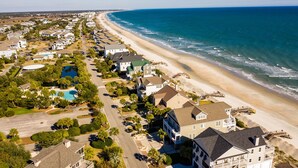 An aerial view of a coastal residential area with houses, a beach, and a swimming pool.