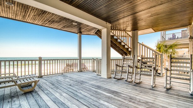 A wooden deck with a railing overlooking a beach, a staircase, and a bench.