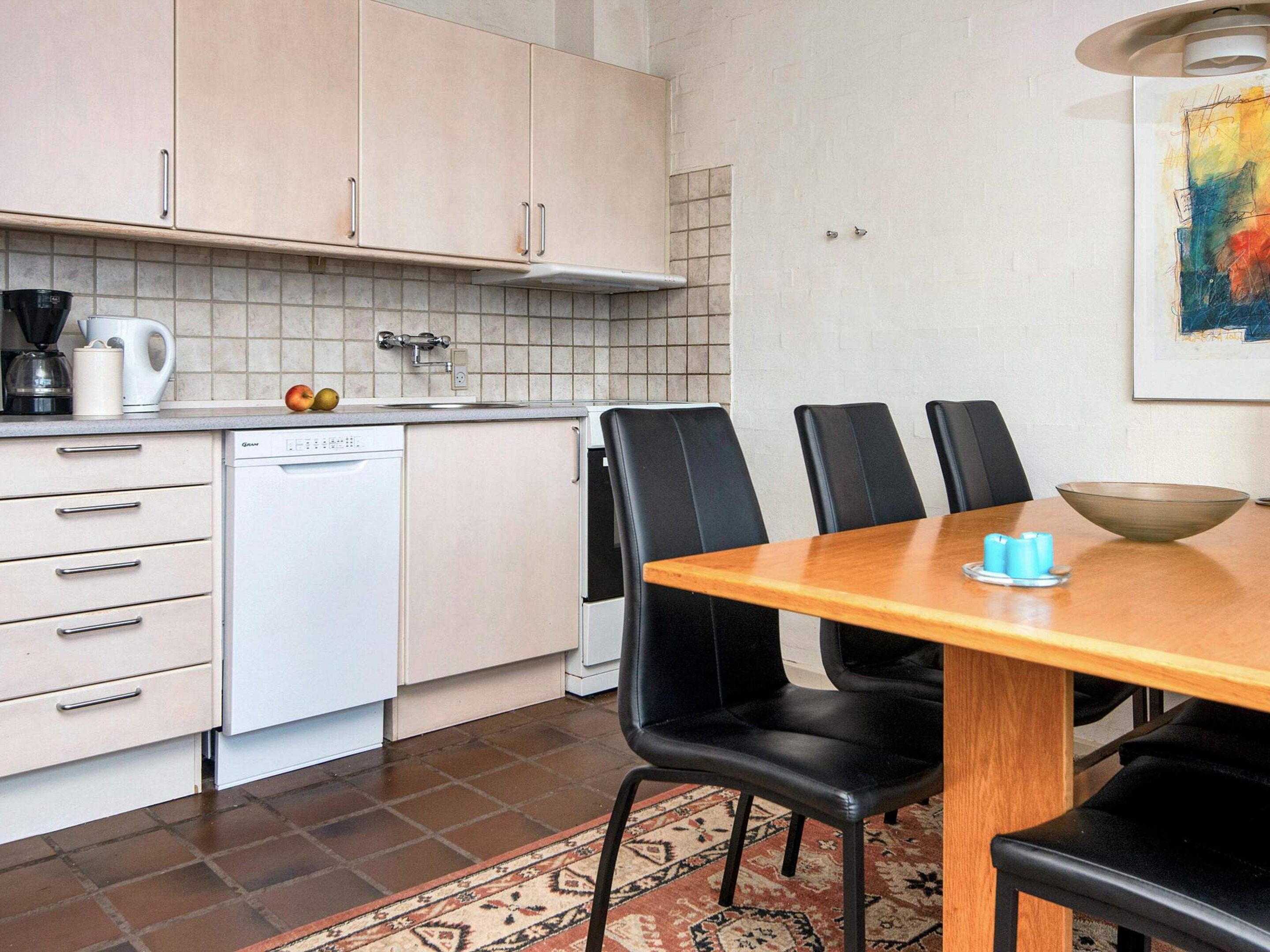 A compact kitchen with a dishwasher, a coffee maker, and a dining table with chairs.
