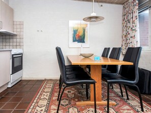A compact kitchen with a dining area, featuring a wooden table, black chairs, a rug, and a painting on the wall. - Waterfront Holiday Home in Henne near Sea (Henne)
