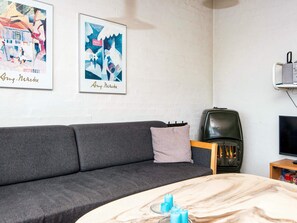 A room with a grey sofa, a small table with candles, a black heater, and two framed artworks on the wall.