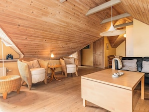 A cozy attic room with wooden floors, a round table, wicker chairs, a sofa, and a ceiling light. - 4 Star Holiday Home in Fur (Fur)