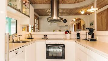 A kitchen with white cabinets, a stainless steel range hood, a built-in oven, and a coffee maker.