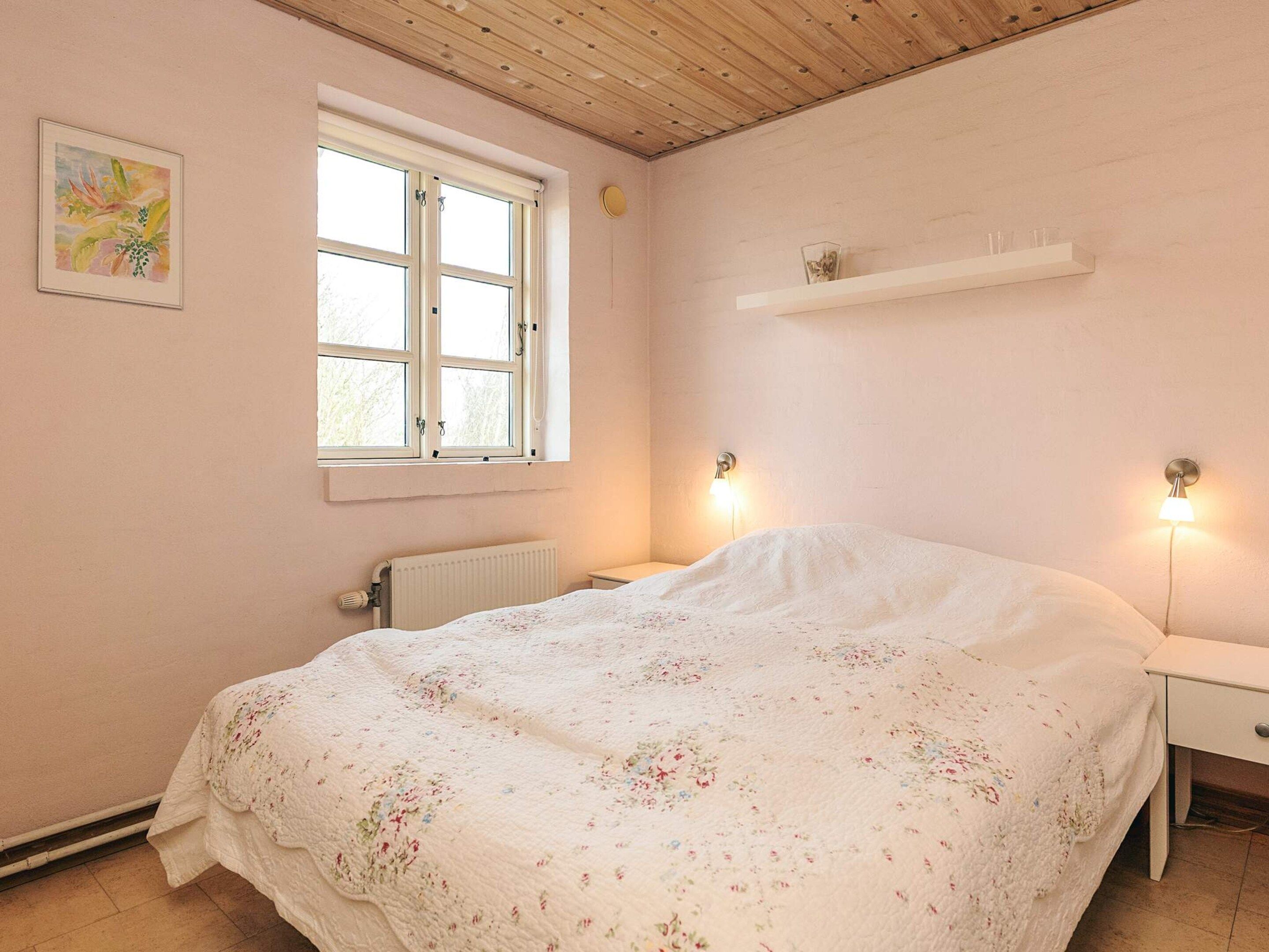 A bedroom with a bed, a window, a radiator, and a wall-mounted shelf.