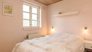 A bedroom with a bed, a window, a radiator, and a wall-mounted shelf.