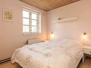 A bedroom with a bed, a window, a radiator, and a wall-mounted shelf.