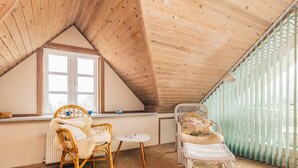 A cozy attic room with wooden floors, a sloped ceiling, and a large window. There are two wicker chairs and a small round table. - 4 Star Holiday Home in Fur (Fur)