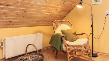 A cozy room with a sloped ceiling, a wicker chair with a cushion, a floor lamp, and a radiator.
