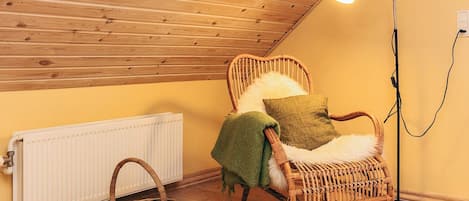 A cozy room with a sloped ceiling, a wicker chair with a cushion, a floor lamp, and a radiator.