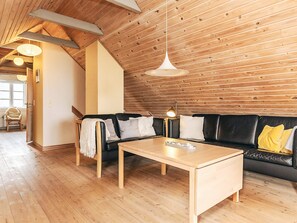 A cozy living room with a wooden ceiling, a black leather sofa, a wooden coffee table, and a hanging light fixture. - 4 Star Holiday Home in Fur (Fur)