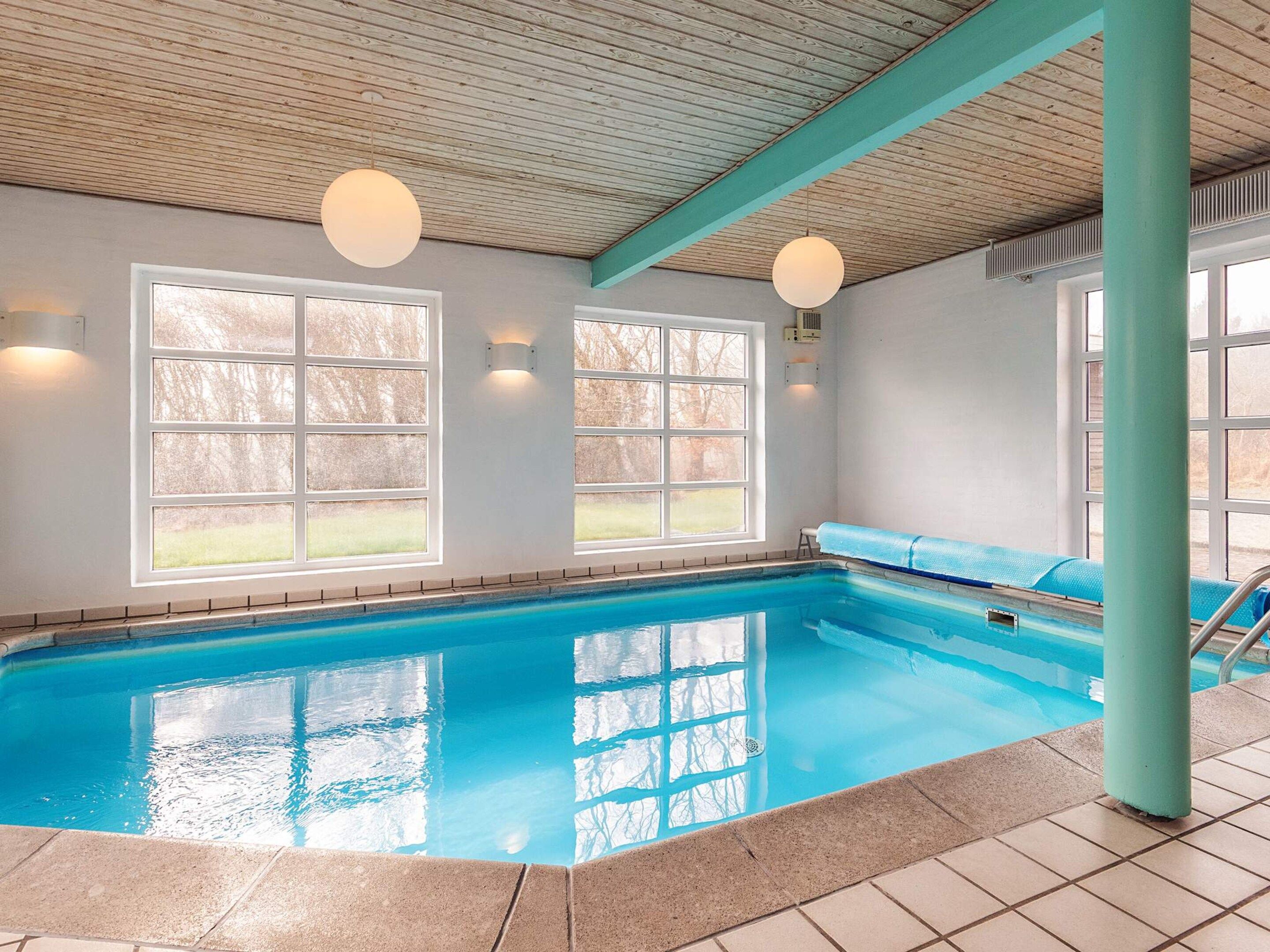 An indoor swimming pool with clear blue water, large windows, and a wooden ceiling.