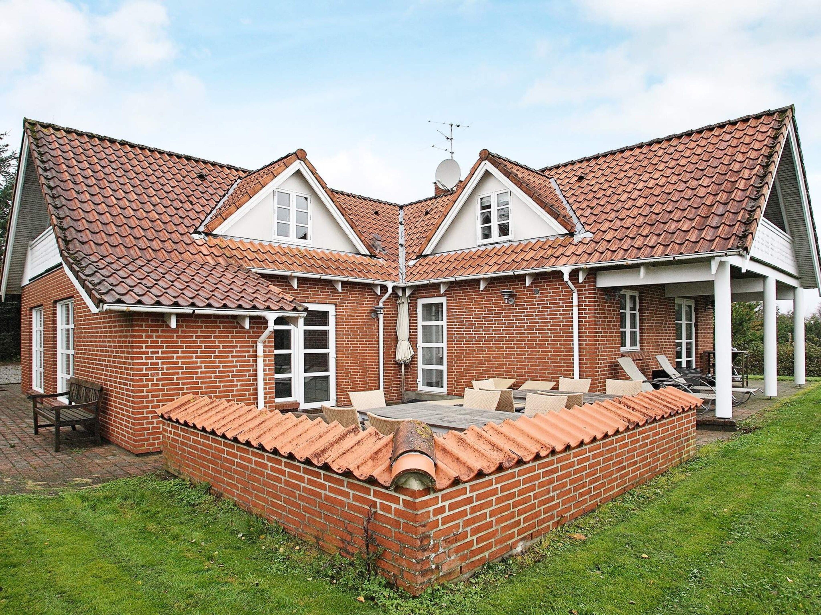 Een woonhuis met twee verdiepingen, een bakstenen gevel, een pannendak en een kleine patio met tuinmeubilair.