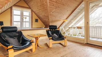 A cozy attic room with wooden floors and a sloped ceiling, featuring two leather chairs and a small table.