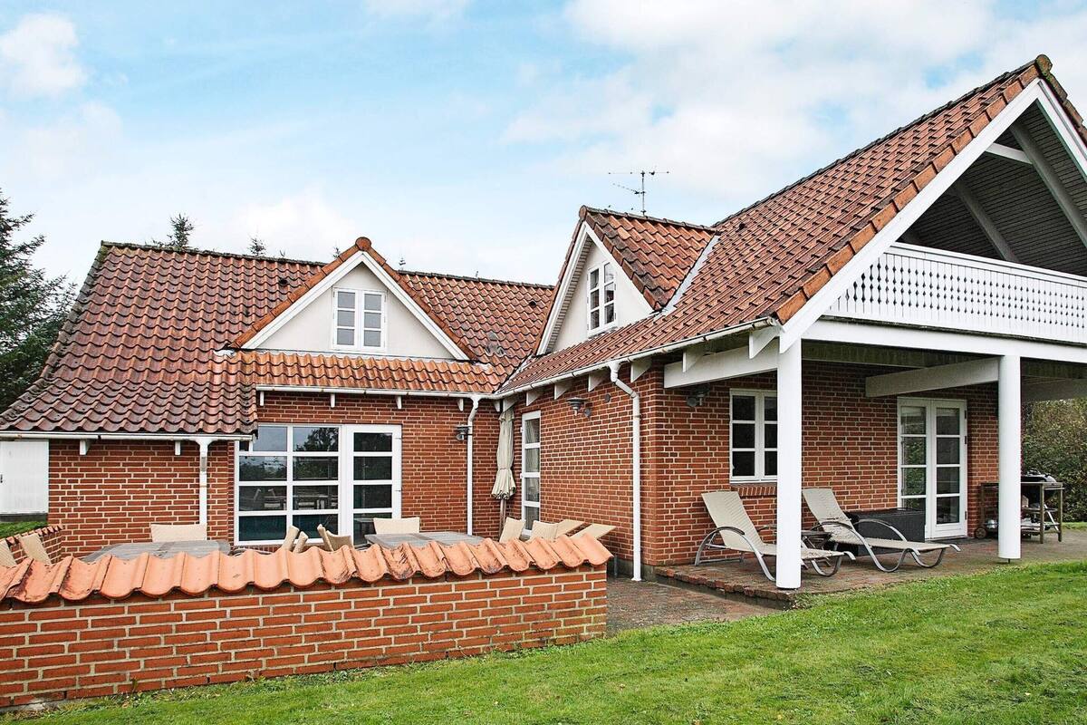 A two-story brick house with a tiled roof, a covered porch with outdoor seating, and a brick wall surrounding the property.