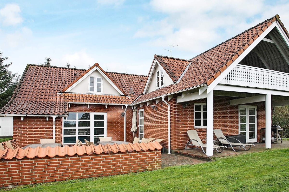 A two-story brick house with a tiled roof, a covered porch with outdoor seating, and a brick wall surrounding the property.