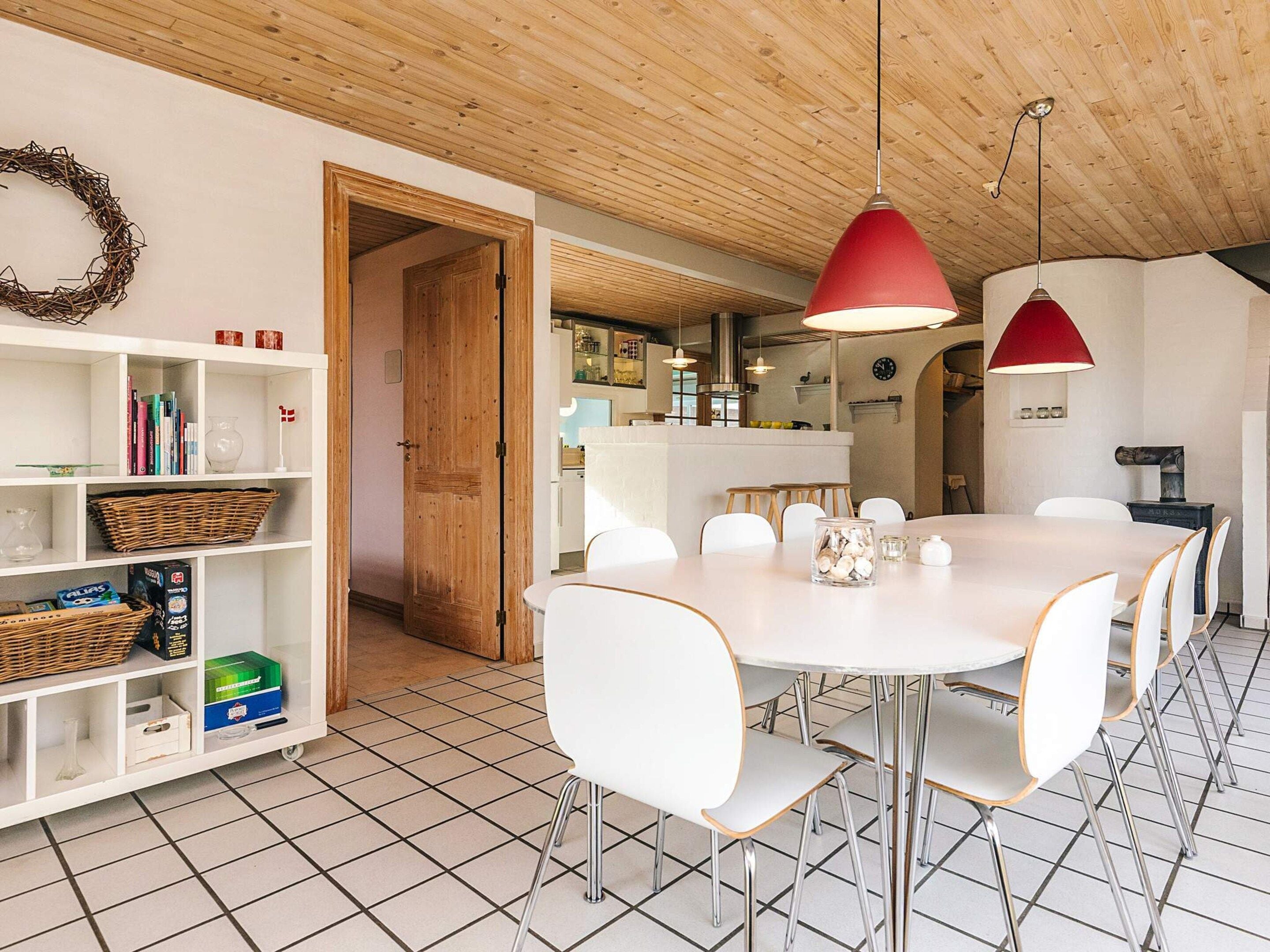 A modern kitchen with a round dining table, white chairs, and a red pendant light.