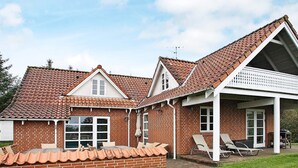 A two-story brick house with a tiled roof, a covered porch with outdoor seating, and a brick wall surrounding the property. - 4 Star Holiday Home in Fur (Fur)