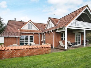 A two-story brick house with a tiled roof, a covered porch with outdoor seating, and a brick wall surrounding the property. - 4 Star Holiday Home in Fur (Fur)
