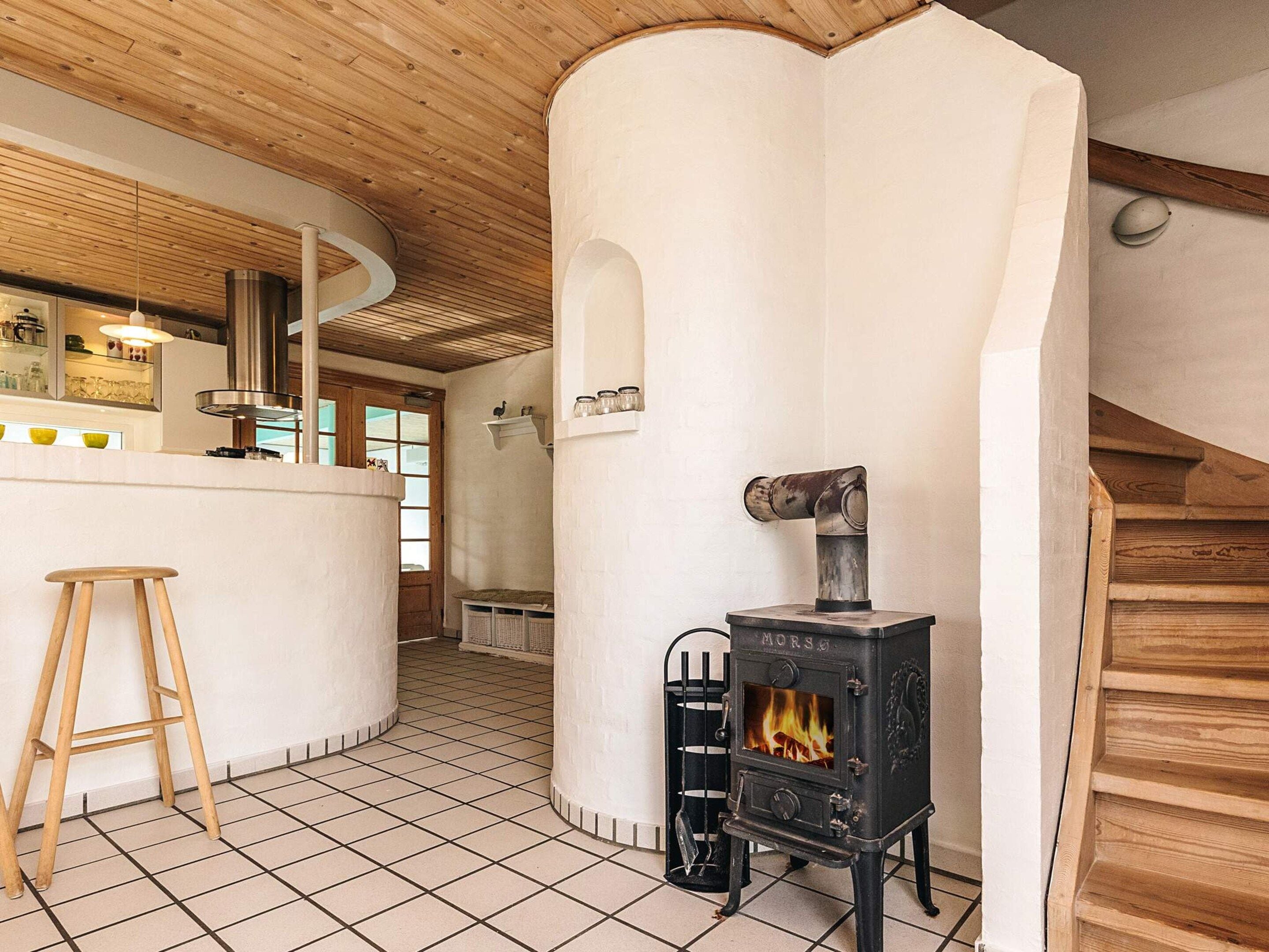 Una cocina con una isla central, un taburete de madera, una estufa y una pared de ladrillo blanco.