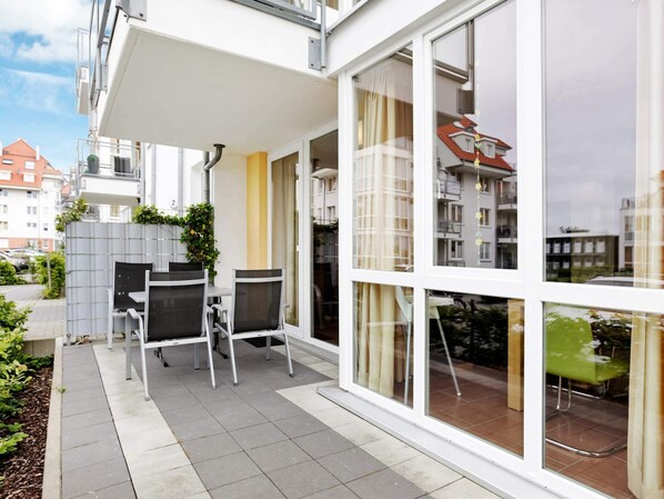 Eine moderne Wohnung mit einer Terrassenfläche, komplett mit Tisch und Stühlen, großen Fenstern und Blick auf die Nachbargebäude.