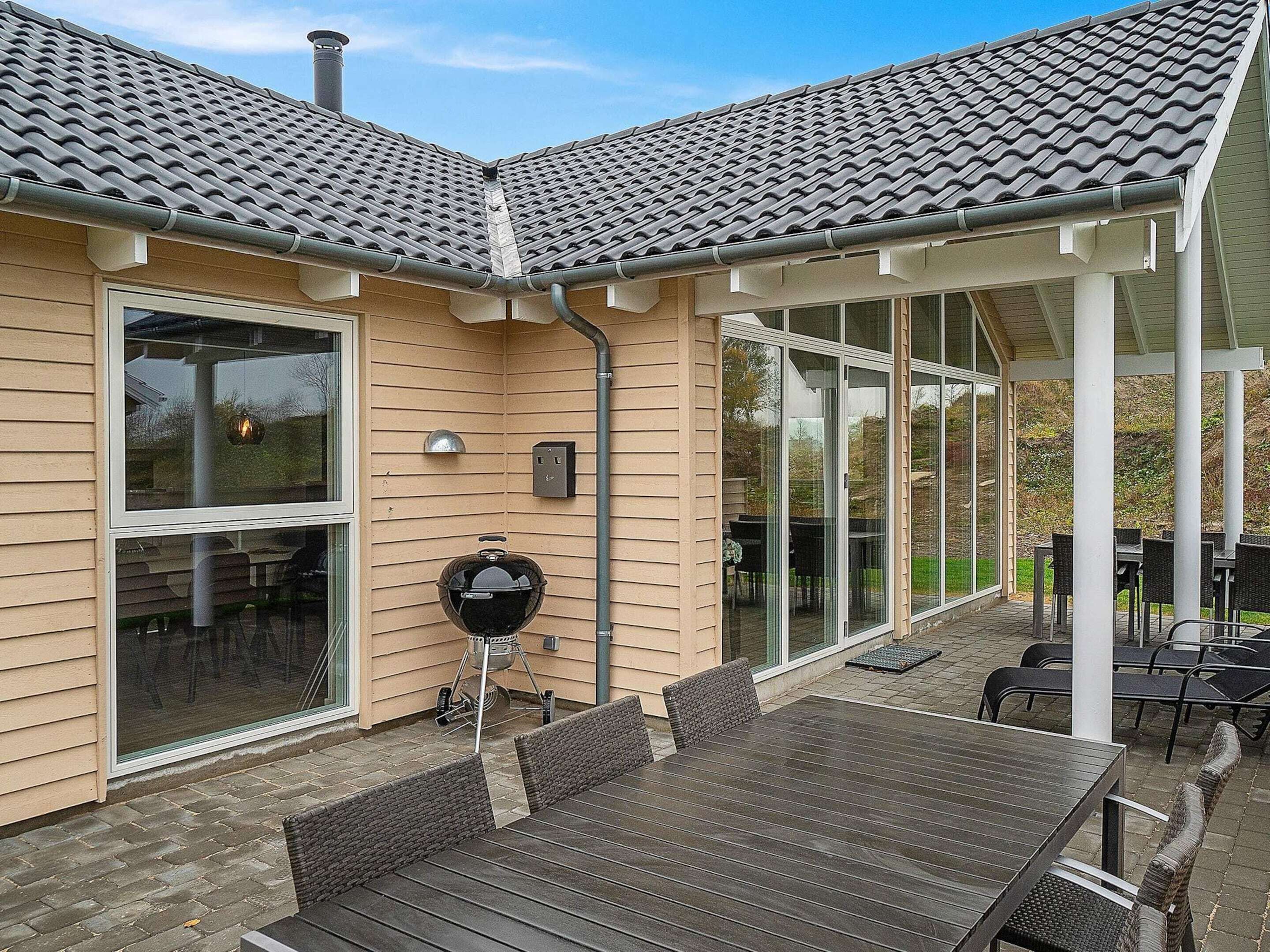 A covered patio with a grill, outdoor seating, and large windows.