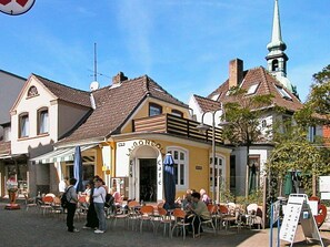 Un café avec une terrasse, une entrée bien visible et le clocher d’une église en arrière-plan.