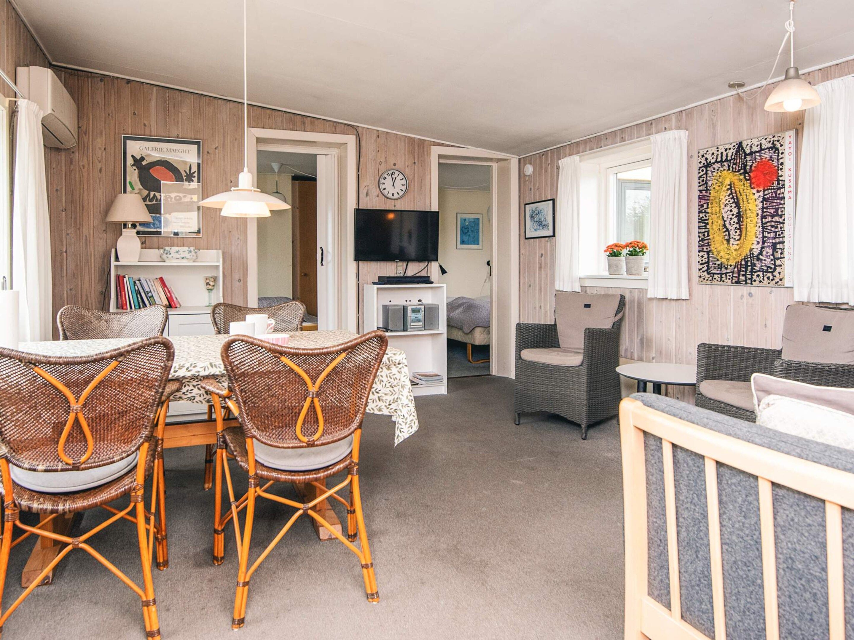 Una sala de estar acogedora con mobiliario de mimbre, una zona de comedor con mesa y sillas, y un televisor montado en la pared.