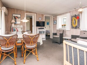 A cozy living room with wicker furniture, a dining area with a table and chairs, and a television mounted on the wall.