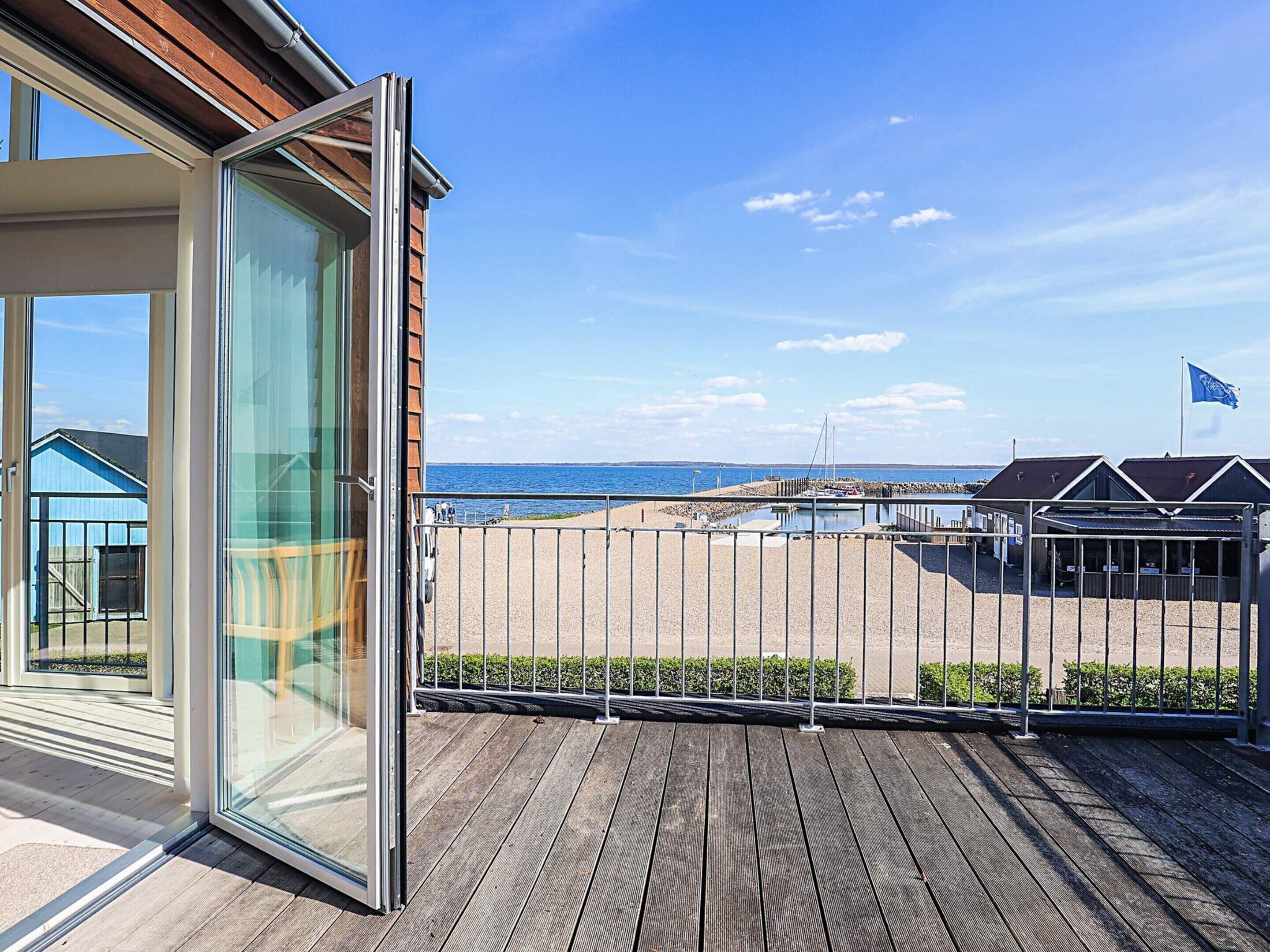 Un balcon avec vue sur la mer, une terrasse en bois et un bâtiment doté d’une porte en verre.