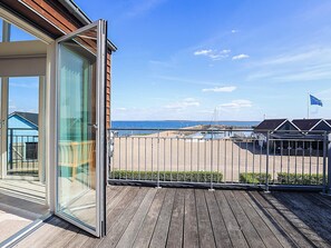 A balcony with a view of the sea, a wooden deck, and a building with a glass door.