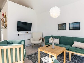 A modern living room with a flat-screen TV, a green sofa, a wooden coffee table, and a white armchair.