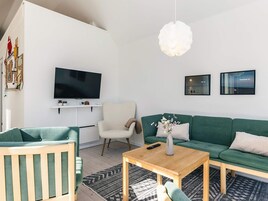 Una sala de estar moderna con una televisión de pantalla plana, un sofá verde, una mesa de centro de madera y un sillón blanco.
