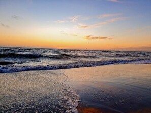 Una playa con olas, cielo despejado y un atardecer.