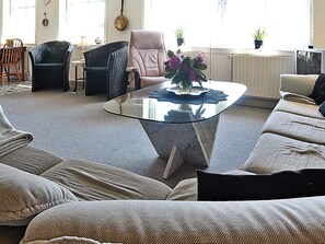 A living room with a glass coffee table, a sofa, a chair, and a small table with a vase of flowers. - 6 Person Holiday Home in Hvide Sande-by Traum (Hvide Sande)