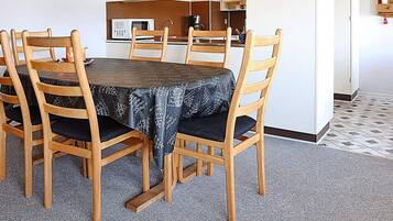 Un comedor con una mesa redonda, seis sillas de madera, un mantel estampado y una cocina al fondo.