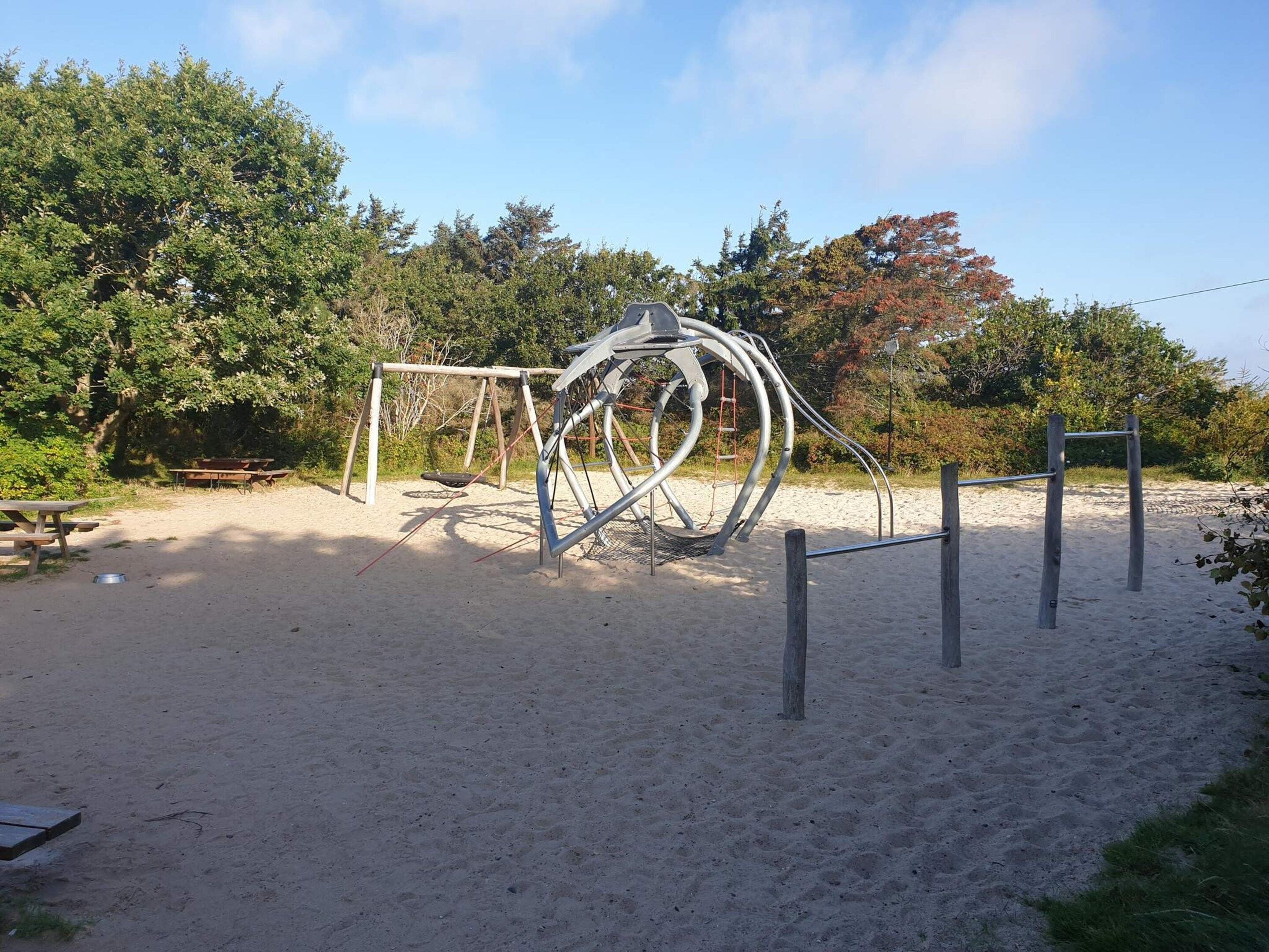 A playground with a metal sculpture, sand, and picnic tables.