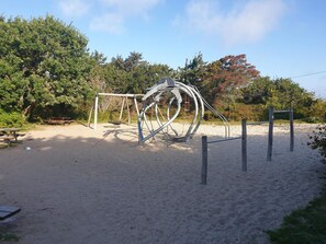 Un parque infantil con una escultura de metal, arena y mesas de picnic.