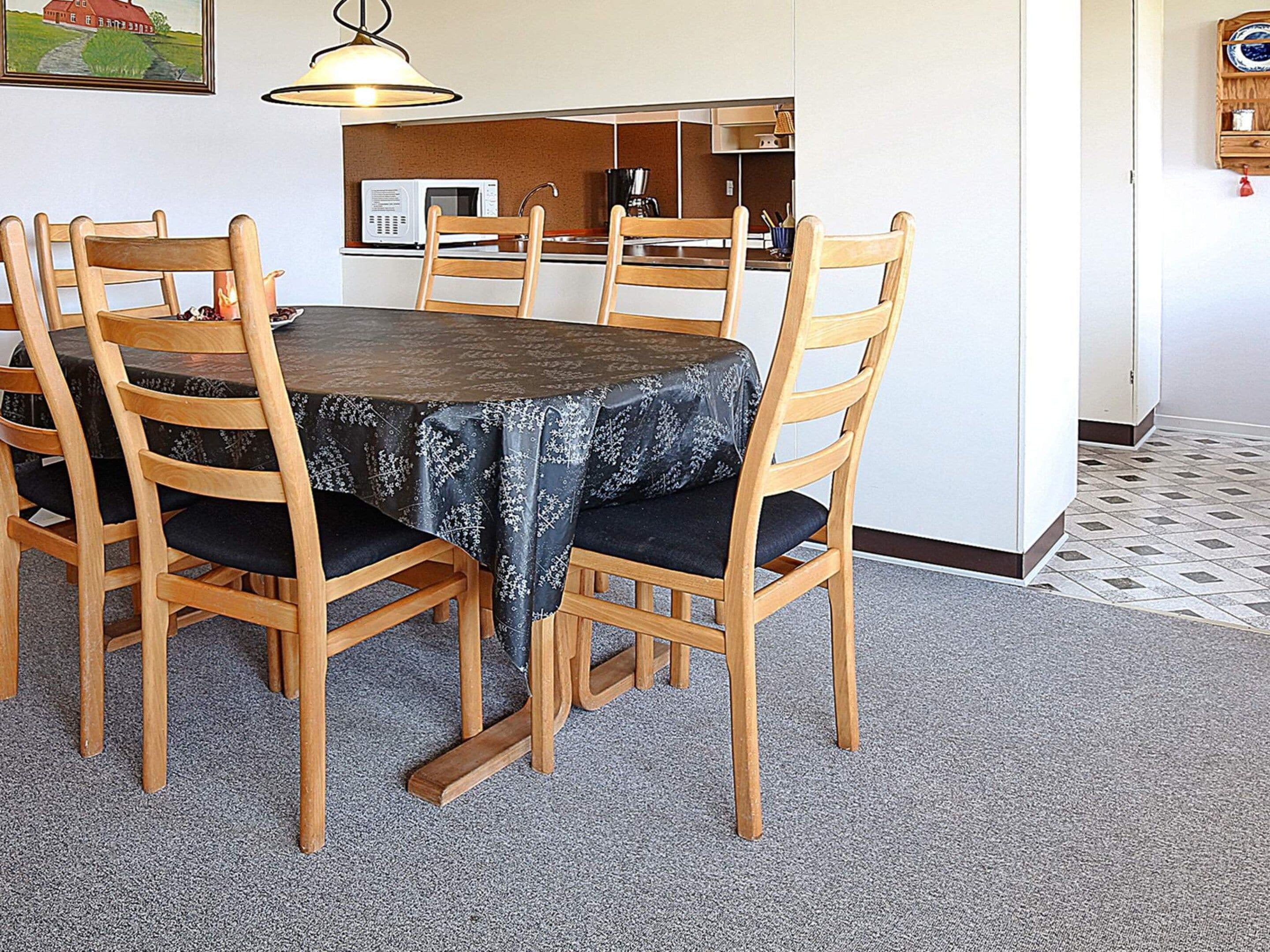 A dining area with a round table, wooden chairs, and a patterned tablecloth.