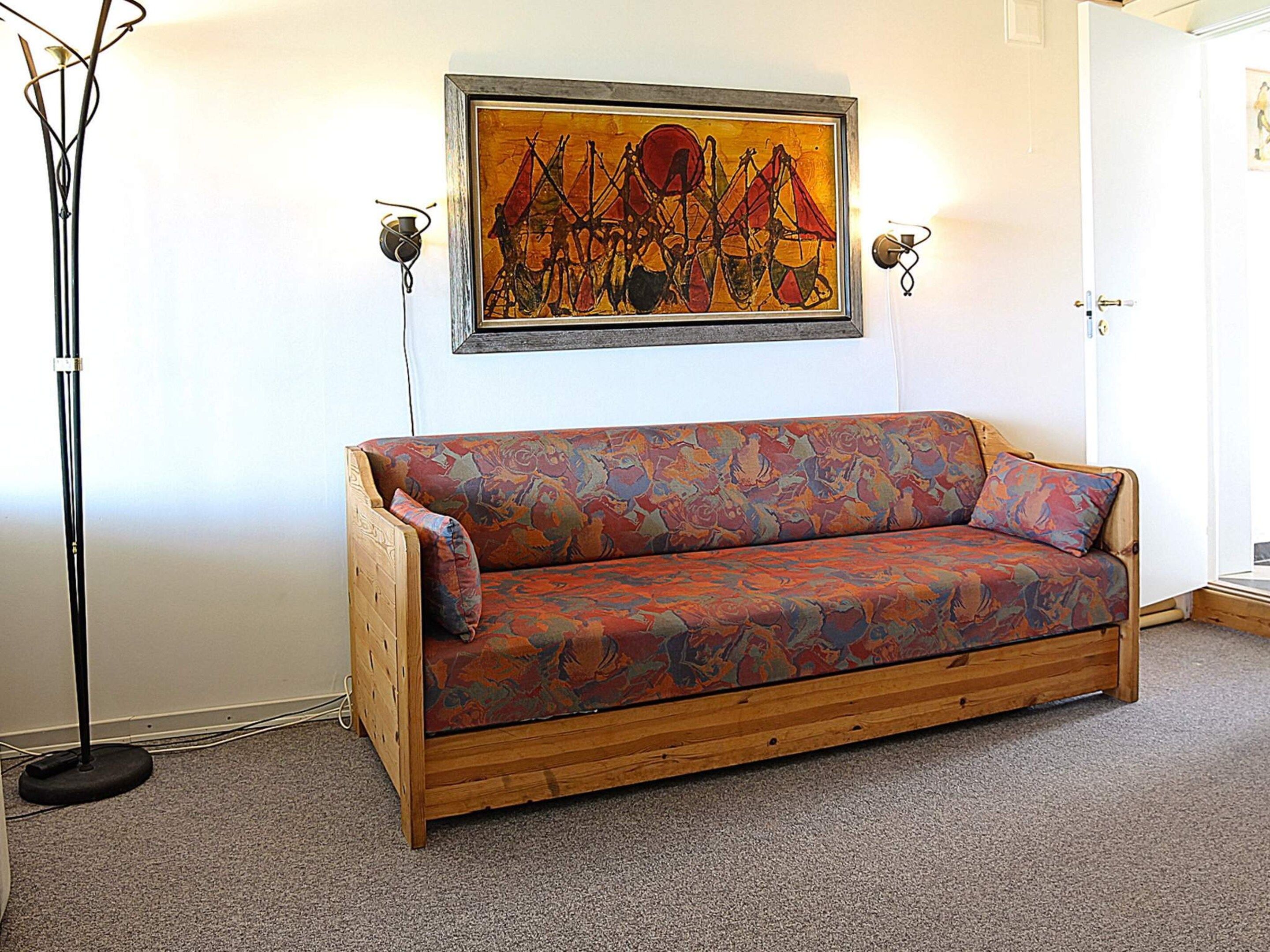 A wooden sofa with a colorful patterned cover, a floor lamp, and a framed abstract painting on the wall.