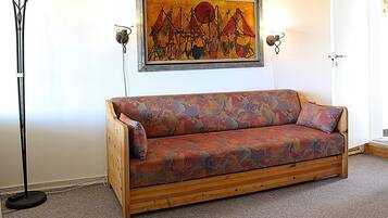 A wooden sofa with a colorful patterned cover, a floor lamp, and a framed abstract painting on the wall.