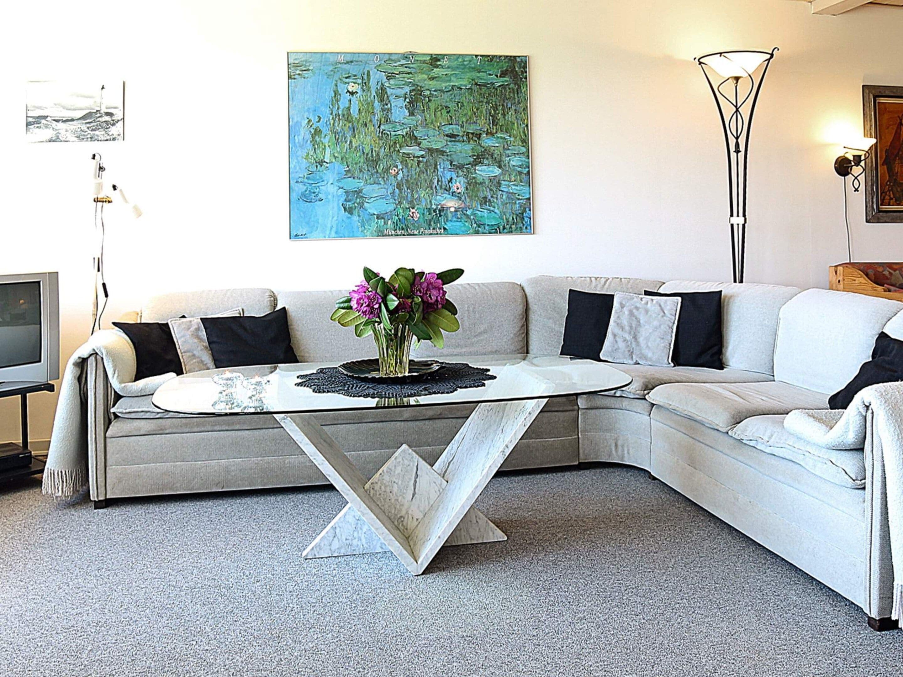 Una sala de estar con un sofá modular, una mesa de centro con un florero, un cuadro en la pared, una lámpara de pie y un televisor.