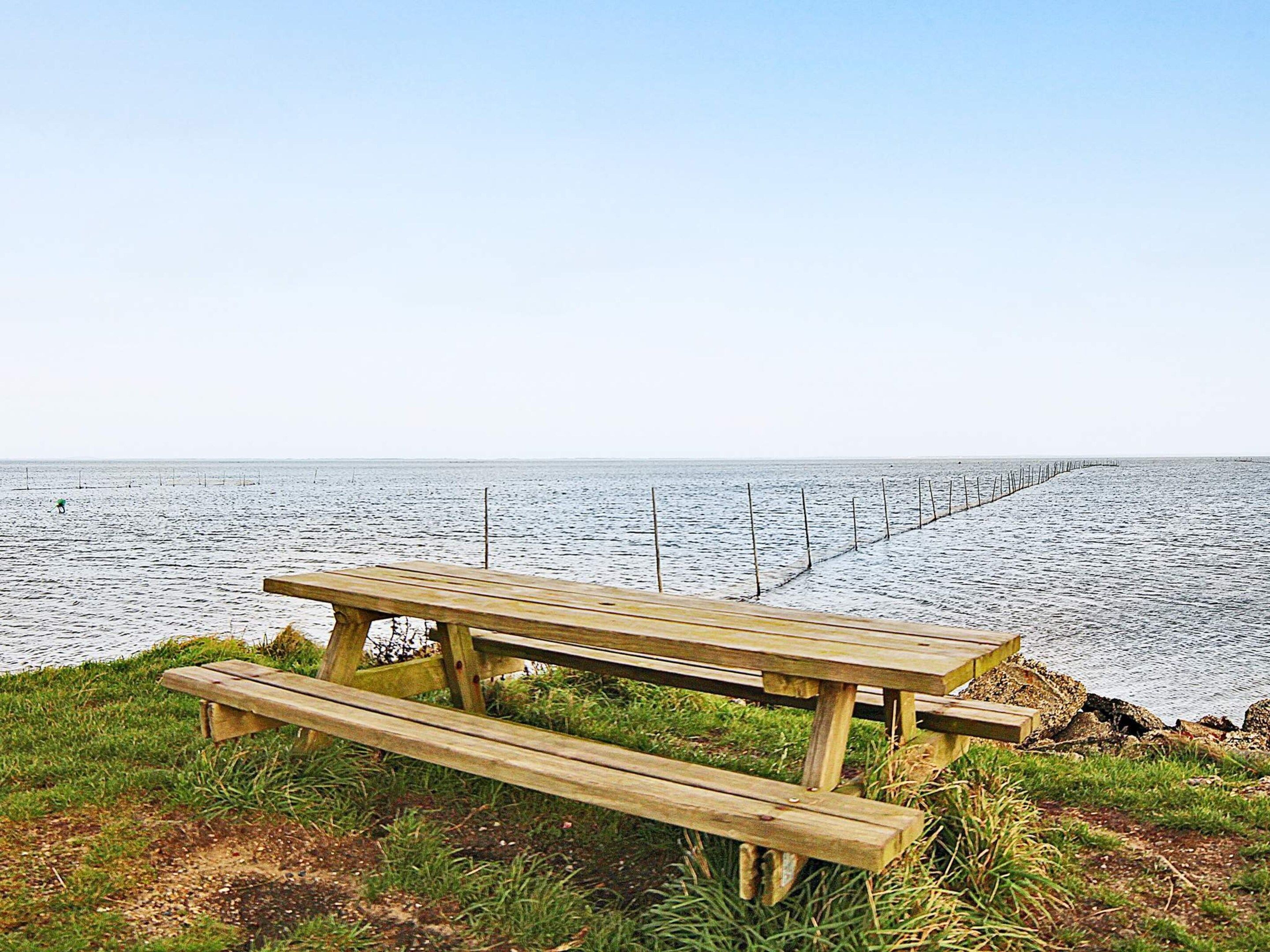 A wooden picnic table with benches overlooking a calm body of water.