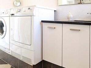 A modern laundry area with a front-loading washer and dryer, a countertop with a soap dispenser, and white cabinetry.