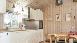 Une cuisine moderne avec des meubles blancs, une table à manger en bois et un panneau décoratif au mur.