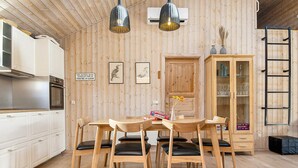 Une pièce aux murs lambrissés, comprenant une table à manger, des chaises, un buffet et une échelle.