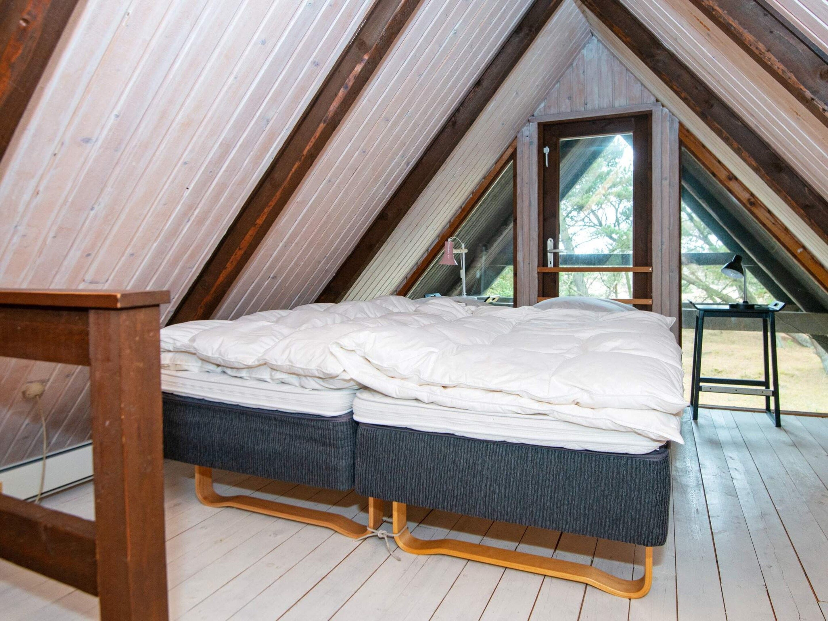 Ein Schlafzimmer im Mansardenstil mit Holzschräge, einem Bett mit blauer Matratze und einem kleinen Tisch mit Lampe.